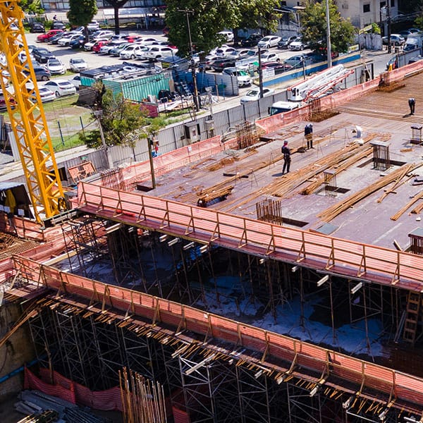 Vista do alto de uma obra, com a laje em concretagem, guindaste amarelo e operários trabalhando